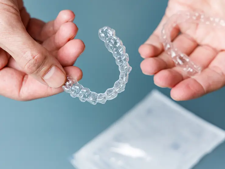 Mãos segurando alinhadores invisíveis removíveis para comer e escovar os dentes